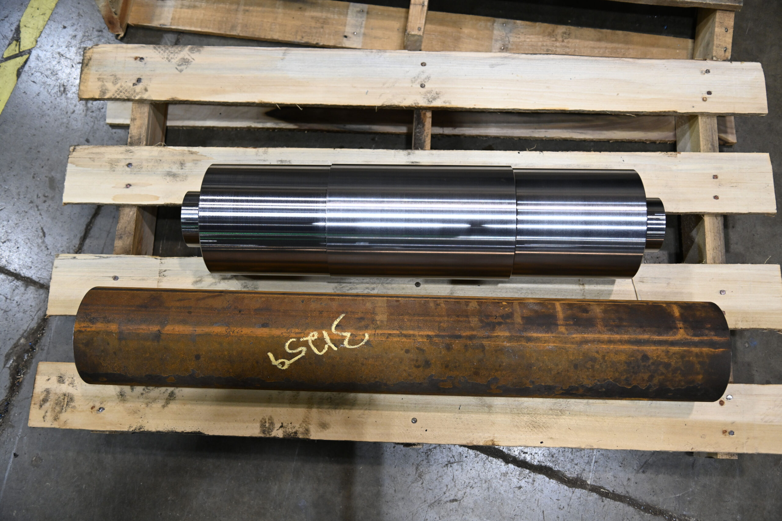 Two metal pieces on a wood pallet, one piece is shiny and metal after it was cleaned and refurbished for use, the other piece is still very rusty